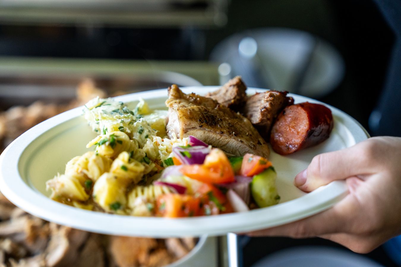 A full plate of roast pork, chorizo, pasta salad and fresh tomato salad